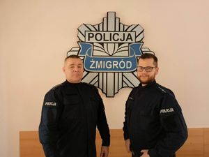 Dwóch policjantów w mundurach stojących przed gwiazdą policyjną z napisem Żmigród