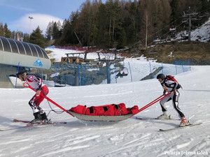 Na zdjęciu para zawodników podczas zawodów narciarskich przewożąca na noszach poszkodowanego.