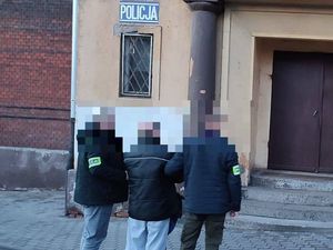 Trzy osoby stojące przed budynkiem z napisem Policja