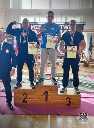 Na zdjęciu trzech mężczyzn  z medalami i dyplomem stojących na podium.