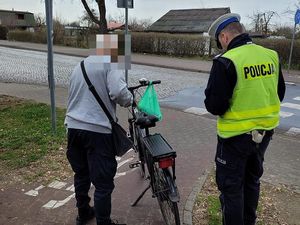 Na zdjęciu policjant w kamizelce odblaskowej poucza mężczyznę stojącego przy rowerze.