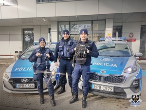 Na zdjęciu policjantka i dwóch policjantów na tle dwóch radiowozów.
