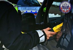 Na zdjęciu policjant mierzy alkomatem poziom alkoholu w wydychanym powietrzy kierowcy siedzącemu w samochodzie.