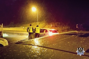 Na zdjęciu dwaj policjanci w porze wieczornej kontrolują kierowcę samochodu osobowego.