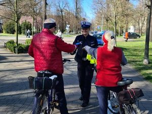 na dworze policjantka i dwie osoby w czerwonych kurtkach na rowerze