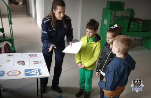 Na zdjęciu widzimy policjantkę, która rozmawia z dziećmi o udzielaniu pierwszej pomocy. Dzieci tłumaczą jakie czynności należy wykonać przy udzielaniu pierwszej pomocy.
