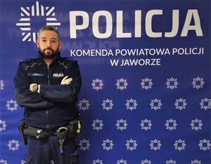 Umundurowany policjant na tle ścianki z napisem Komenda Powiatowa Policji w Jaworze