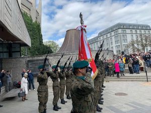 osoby stojące na dworze, w okolicy żołnierze oraz biało-czerwone flagi