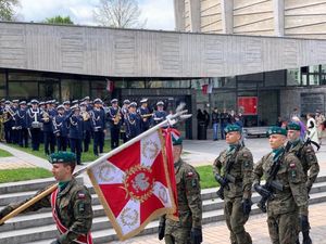 osoby stojące na dworze, w okolicy żołnierze oraz biało-czerwone flagi