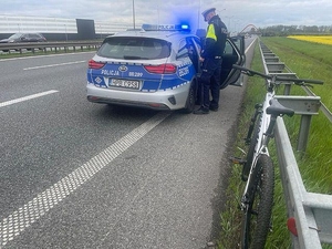 Na autostrada, pobocze i zdjęciu policjant stojący koło radiowozu obok stoi oparty o barierki rower.