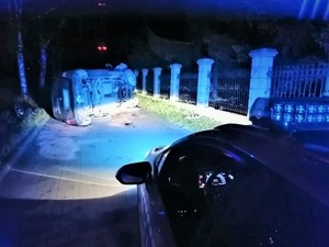 Uszkodzony pojazd leżący na lewym boku i przód oznakowanego radiowozu