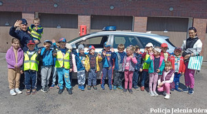 Policjantka i przedszkolaki stoją przed radiowozem