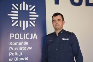 Policjant stoi przy tablicy, na której widnieje napis POLICJA Komenda Powiatowa Policji w Oławie