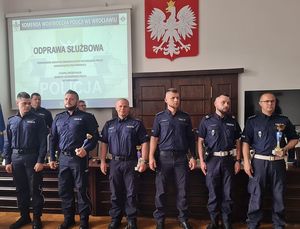 Na zdjęciu nagrodzeni policjanci stojący w szeregu. W tle godło RP.