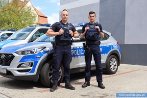 Na zdjęciu dwaj policjanci stojący przy radiowozie.