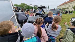 Na zdjęciu dzieci podczas festynu siedzące policyjnej motorówce, w tle radiowóz policyjny i pozostali uczestnicy festynu.