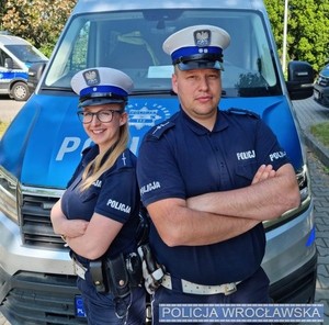 Na zdjęciu policjantka i policjant przy radiowozie.