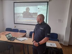 Na zdjęciu policjant spogląda na projektor na którym prezentowany jest materiał filmowy.