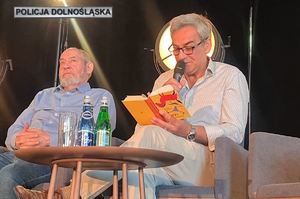Dwóch mężczyzn siedzących w pomieszczeniu, jeden z nich trzyma mikrofon i książkę