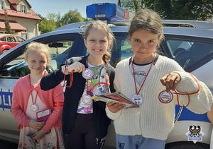 Na zdjęciu trzy dziewczynki przy radiowozie trzymające znaczki wzorowy kierowca.