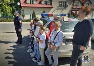 Na zdjęciu policjant z dziećmi przy radiowozie z opiekunką