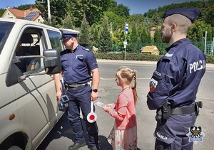 Na zdjęciu dwaj policjanci  z dziewczynką kontrolują pojazd