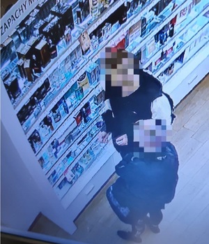 Na zdjęciu kobieta stojąca przy stoisku z perfumami, zdjęcie z kamery monitoringu.