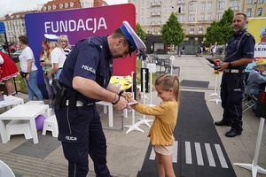 Na zdjęciu policjant zakłada dziewczynce opaskę odblaskową.