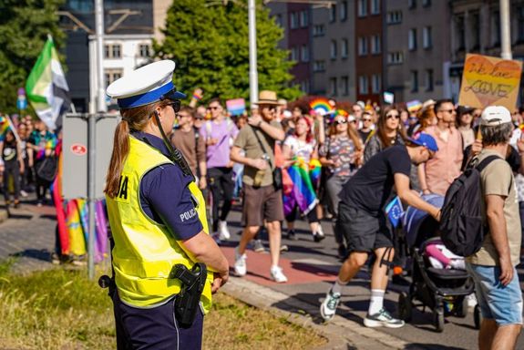 stojąca przy drodze policjantka ruchu drogowego, w tle idąca duża grupa ludzi