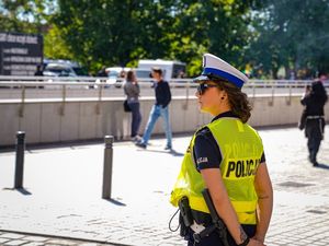 stojąca przy drodze policjantka ruchu drogowego w odblaskowej kamizelce i białej czapce