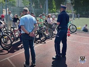 Na zdjęciu policjant i egzaminator instruują dzieci podczas egzaminu na kartę rowerową.