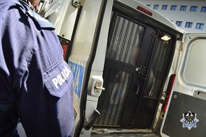 Na zdjęciu widać rękę policjanta w mundurze i tył radiowozu z otwartymi drzwiami tylnymi