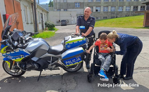 Na zdjęciu widać policyjny motocykl, dwoje policjantów i chłopca na wózku