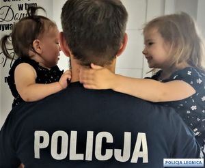 Policjant stojący tyłem obejmuje dwie małe córeczki.