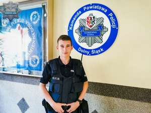 Policjant w tle logo i  napis Komenda Powiatowa Policji Kamienna Góra.