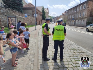 Dwaj policjanci stojący przy ulicy i dzieci stojące na chodniku.
