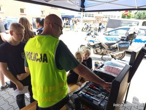 Policjant prezentuje dzieciom sprzęt policyjny znajdujący się w walizce.