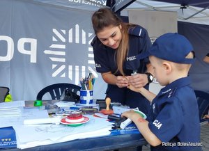 Policjantka pokazuje chłopcu jak pobiera się odciski palców.