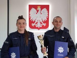 Policjantka i policjant z dyplomami i pucharem. W tle godło Polski.