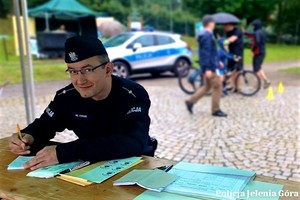 Policjant wypełniajmy dokumenty na stoisku policyjnym podczas festynu.