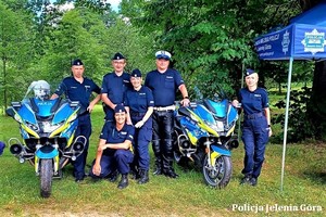 Policjantki i policjanci biorący udział w festynie, stojący przy dwóch motorach policyjnych.