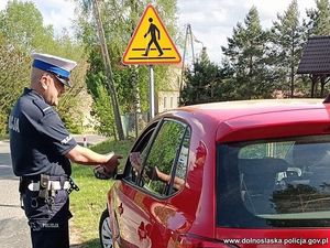 Policjant stoi przy samochodzie osobowym i sprawdza prawo jazdy kierującego.