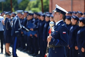 Dyrygent orkiestry policyjnej w tle nowo przyjęci policjanci.