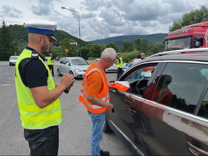 policjanci i osoby w pomarańczowych kamizelkach stojące przy samochodach przy drodze