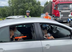policjanci i osoby w pomarańczowych kamizelkach stojące przy samochodach przy drodze