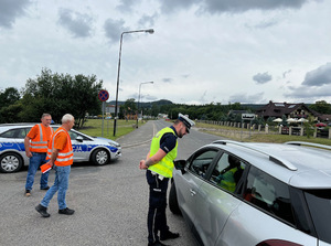 policjanci i osoby w pomarańczowych kamizelkach stojące przy samochodach przy drodze