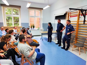 w pomieszczeniu policjanci stojący na przeciwko osób siedzących