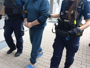 policjanci na dworze z osobą w niebieskim dresie i kajdankach