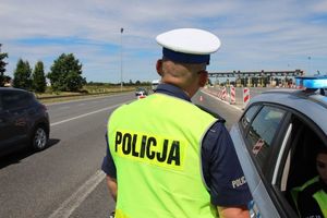 Policjant stojący przy radiowozie na autostradzie obserwuje jadące samochody.