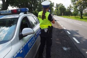 Policjantka stojąca przy radiowozie mierząca prędkość nadjeżdżającemu z naprzeciwka pojazdowi osobowemu.